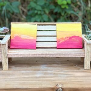 A miniature Cedar Bench that is holding two miniature paintings.